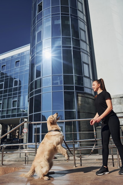 Una joven positiva se divierte y hace trucos con su perro cuando camina al aire libre cerca del edificio comercial