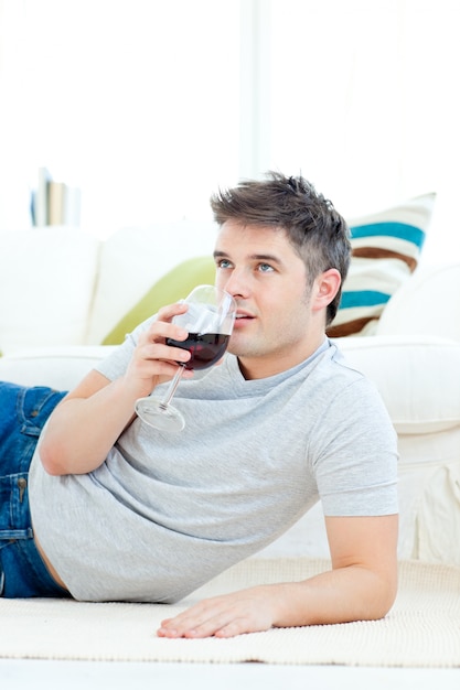 Joven positivo bebiendo vino en la sala de estar