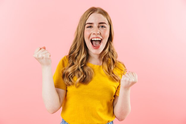 un joven positivo feliz gritando linda chica aislada sobre la pared rosa que muestra el gesto del ganador.