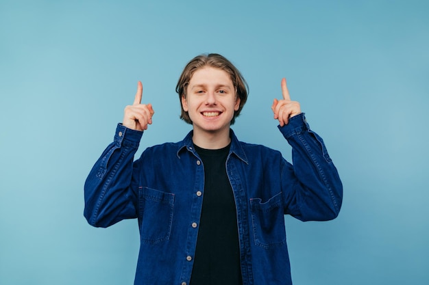 Un joven positivo con ropa informal se para en un fondo azul con una sonrisa en la cara