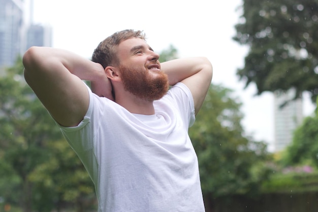 Joven positivo sonriendo durante la lluvia en el parque hombre alegre disfrutando de la lluvia al aire libre chico