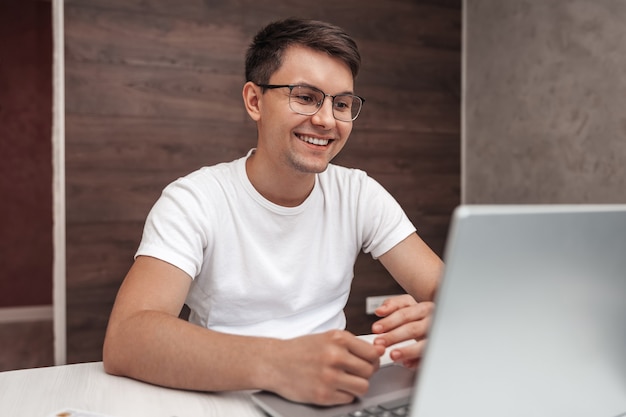 Foto joven positivo con una sonrisa se ve en una computadora portátil