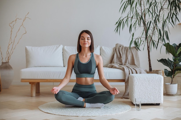 Una joven practica yoga en casa en chándal Sentada en posición de loto