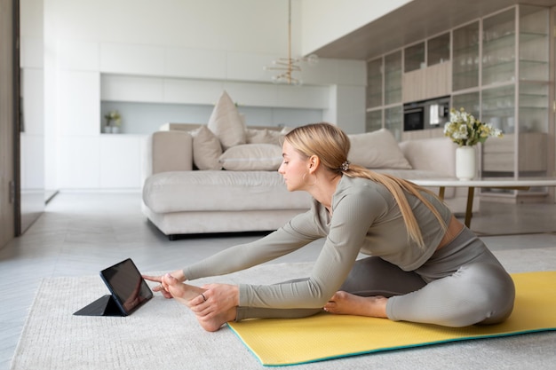 Joven practica yoga en casa con tablet pc