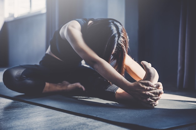 Joven practicando yoga en clase; Hermosa chica sintiendo tranquilidad y relax en clase de yoga.