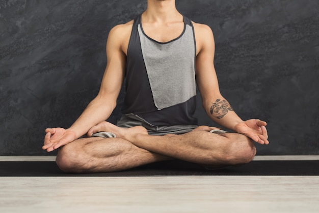 Joven practicando yoga, ejercicios de meditación. Chico hace postura de loto para relajarse, sentado en una colchoneta en el gimnasio. Estilo de vida saludable, espacio de copia, cultivo