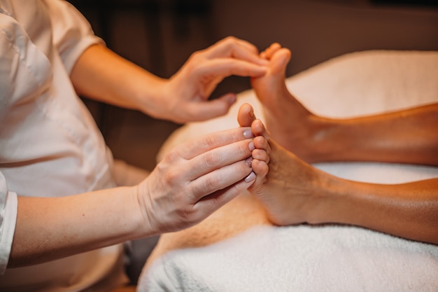 Joven practicante del spa está masajeando los pies de los clientes antes de comenzar el siguiente procedimiento de limpieza