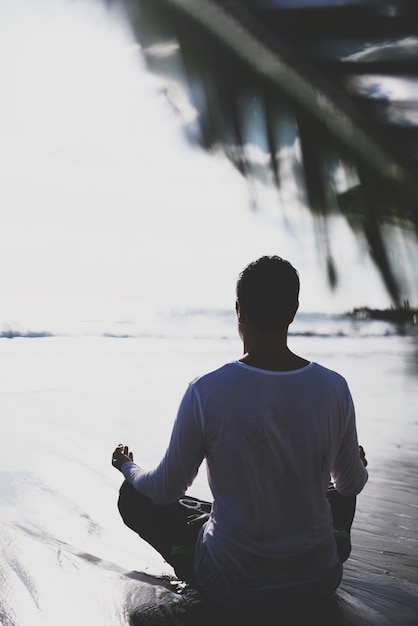 Joven practicar yoga en la playa al atardecer.