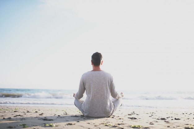 Joven practicar yoga en la playa al atardecer.