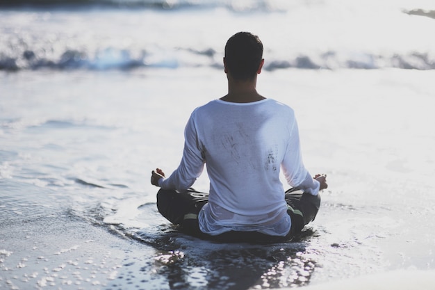 Joven practicar yoga en la playa al atardecer.