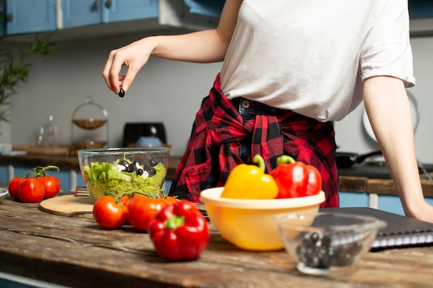 La joven prepara una ensalada vegetariana en la cocina y agrega ingredientes cortados al plato