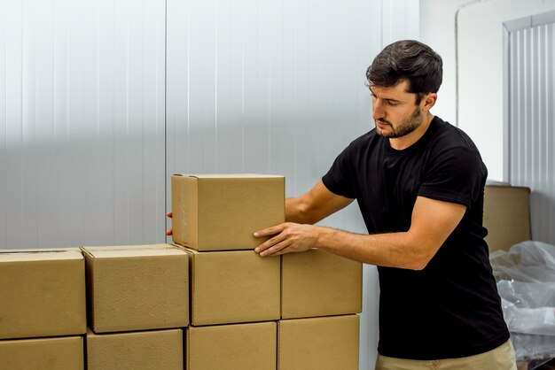 Foto joven preparando envíos en cajas de cartón en una fábrica.