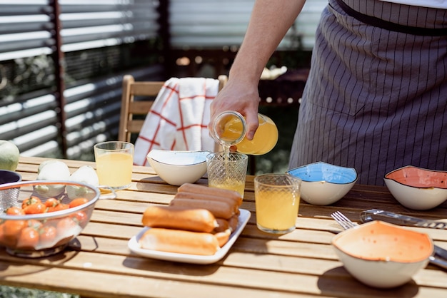 Joven preparando mesa para picnic, sosteniendo una botella con limonada en la soleada tarde de verano. Barbacoa de patio trasero