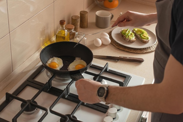 Joven preparando tostadas con aguacate y huevo para desayunar en la cocina