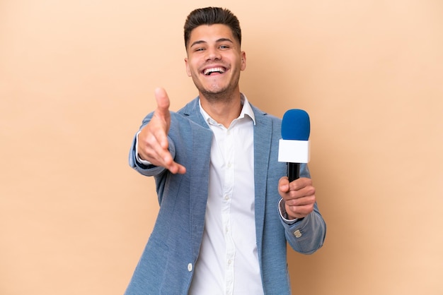 Joven presentador de televisión caucásico aislado de fondo blanco estrechando la mano para cerrar un buen trato