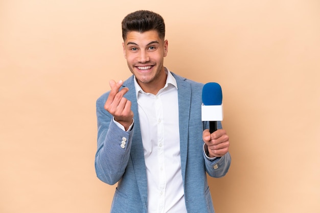 Joven presentador de televisión caucásico hombre aislado sobre fondo blanco haciendo gesto de dinero