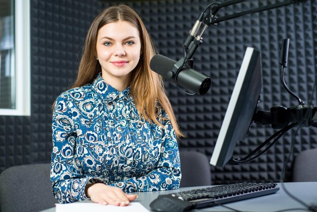 Joven presentadora de radio de mujer bonita sentada en el estudio con auriculares y hablando al aire