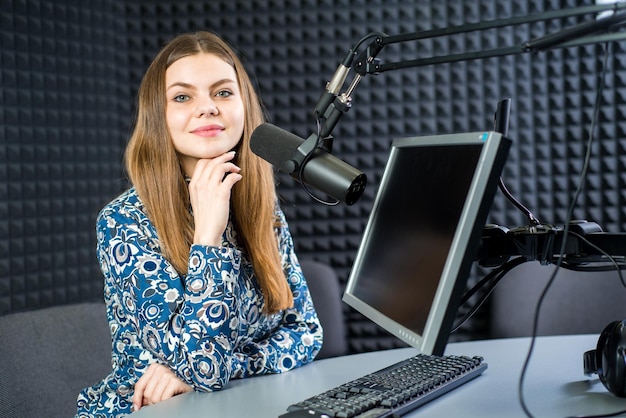 Joven presentadora de radio de mujer bonita sentada en el estudio con auriculares y hablando al aire