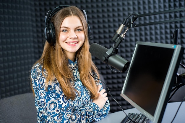 Joven presentadora de radio de mujer bonita sentada en el estudio con auriculares y hablando al aire