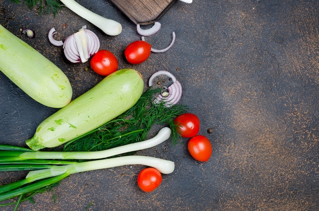 Joven primavera calabacín, tomates, hierbas y especias en superficie negra