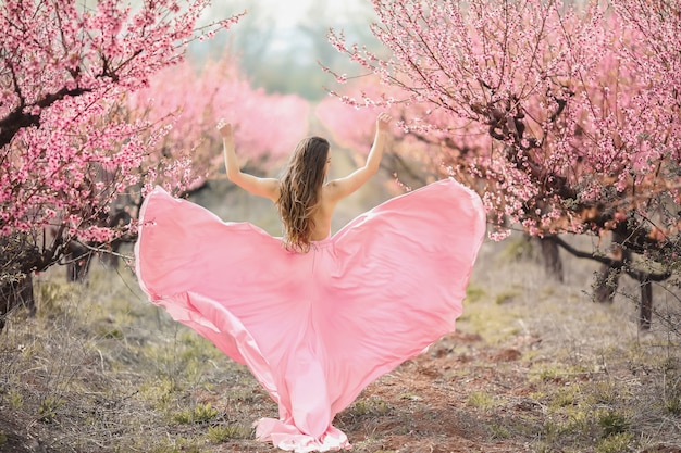 Una joven princesa camina en un jardín floreciente. Chica en un lujoso vestido rosa con un tren. Tonificación de moda.