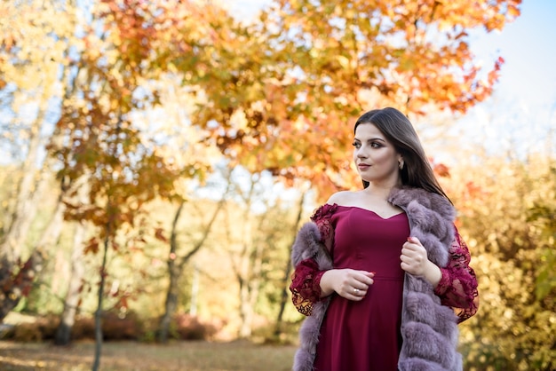 Joven princesa con un hermoso vestido rojo en el parque. El fondo es una naturaleza otoñal brillante y dorada.