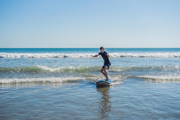 Joven, principiante Surfer aprende a surfear en una espuma de mar en la isla de Bali