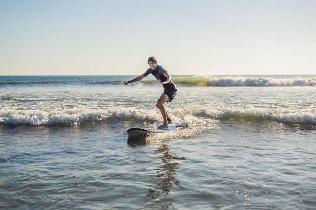 Joven, principiante Surfer aprende a surfear en una espuma de mar en la isla de Bali