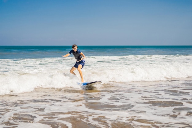 Joven principiante Surfer aprende a surfear en una espuma de mar en la isla de Bali