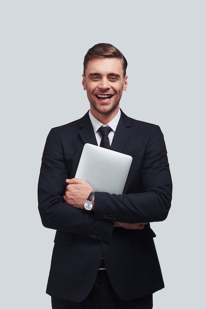 Joven profesional de negocios. Apuesto joven con tableta digital y sonriendo mientras está de pie contra el fondo gris