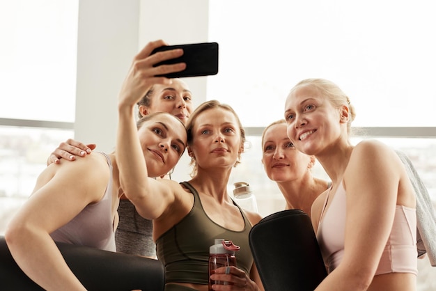 Joven profesor que usa un teléfono inteligente mientras fotografía con estudiantes de yoga después de la clase de yoga