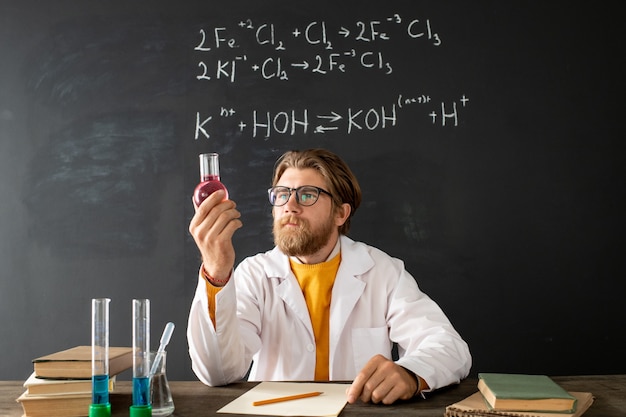 Joven profesor de química contemporánea en bata blanca cruzando los brazos sobre el pecho durante la lección en línea