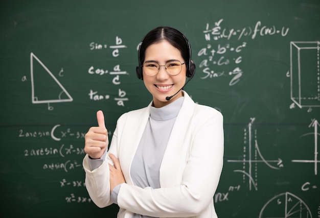 Joven profesora asiática enseñando mostrando los pulgares hacia arriba y videoconferencia con un estudiante mirando la cámara Profesora entrenando las matemáticas en la pizarra del aula del curso en línea