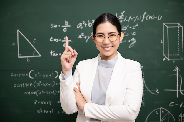 Joven profesora asiática enseñando de pie mostrando el dedo índice y videoconferencia con estudiante mirando la cámara Profesora entrenando las matemáticas en la pizarra del aula del curso en línea