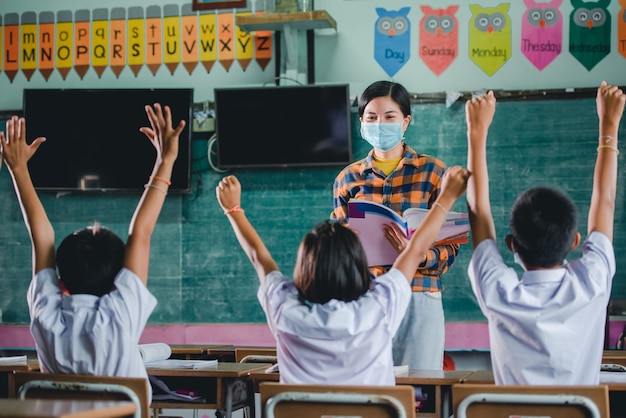 Joven profesora asiática con un rostro médico y los estudiantes en una escuela de la aldea tailandesa rural están aprendiendo