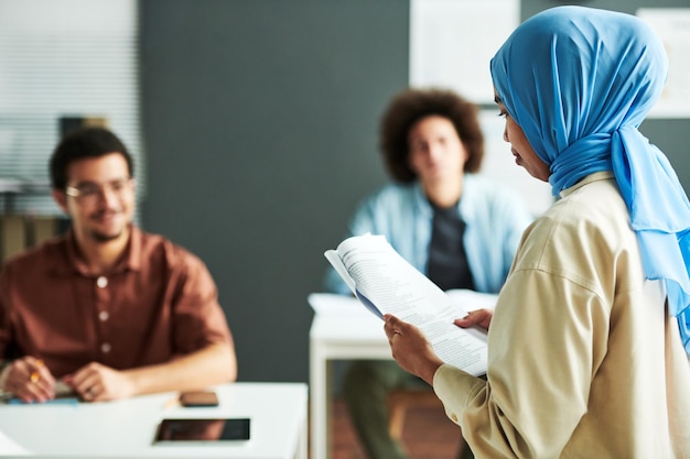 Joven profesora musulmana en hiyab azul mirando el texto en el documento