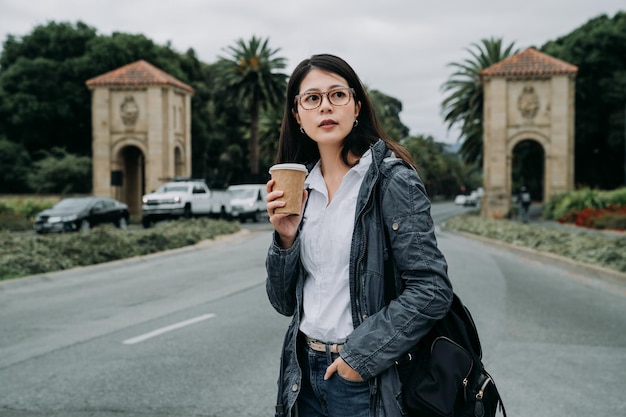 joven profesora que va a trabajar por la mañana a la universidad en stanford Palo Alto California EE.UU. mujer asiática enseñando chino en la escuela sosteniendo una taza de café llevar mochila caminando por la carretera.