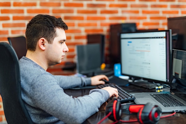 Joven programador inteligente y ambicioso que usa aparatos y trabaja duro en la empresa de TI El programador se concentra en el problema de mirar las pantallas mientras está sentado en la silla