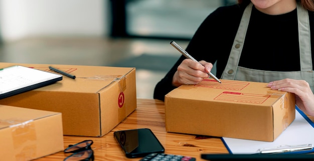 Joven propietaria de una pequeña empresa escribiendo en una caja de paquetes preparando un paquete para su cliente. Empresario de PYME o concepto de estilo de vida independiente.