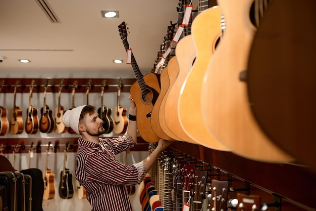 Joven propietario masculino de una tienda de instrumentos musicales que pone la guitarra en la vitrina. Concepto de pequeña empresa y comercio.