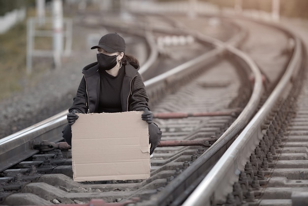 Una joven protestante está sentada en la vía del tren, sosteniendo un cartel con un lugar para firmar.