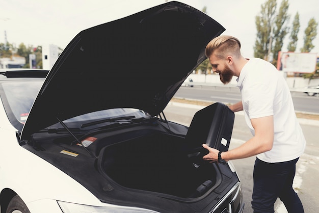 Un joven puso el equipaje en la cajuela de su auto eléctrico.