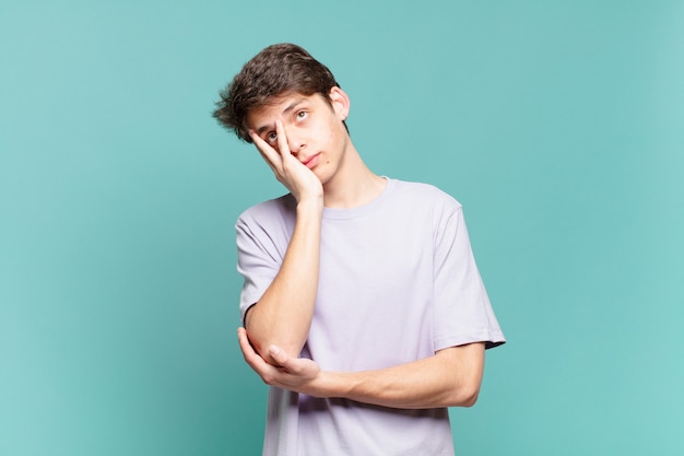 Joven que se siente aburrido, frustrado y con sueño después de una tarea tediosa, aburrida y tediosa, sosteniendo la cara con la mano