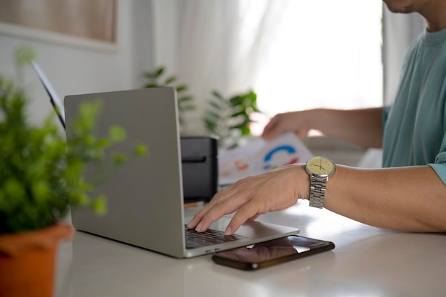 Joven que trabaja desde casa haciendo papeleo mientras usa una computadora portátil investigando una nueva estrategia comercial