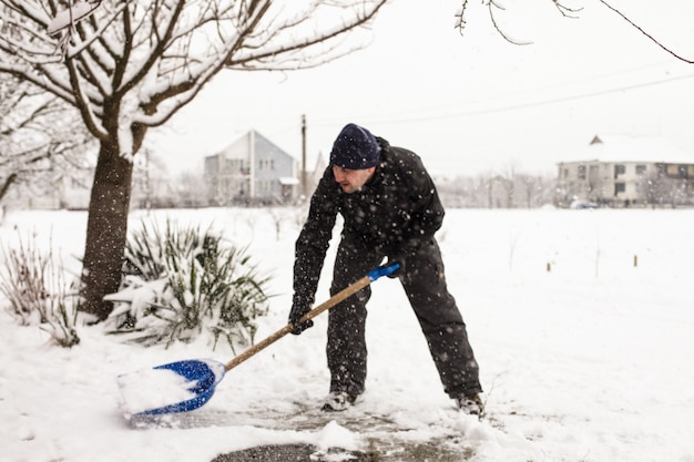 Joven quitar la nieve cerca de la casa suburbana