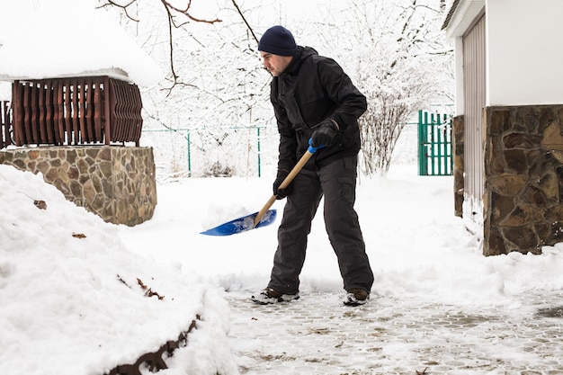 Joven quitar la nieve cerca de la casa suburbana