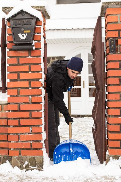 Joven quitar la nieve cerca de la casa suburbana