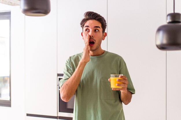 Joven de raza mixta bebiendo jugo de naranja en su cocina está diciendo una noticia secreta de frenado caliente y mirando a un lado