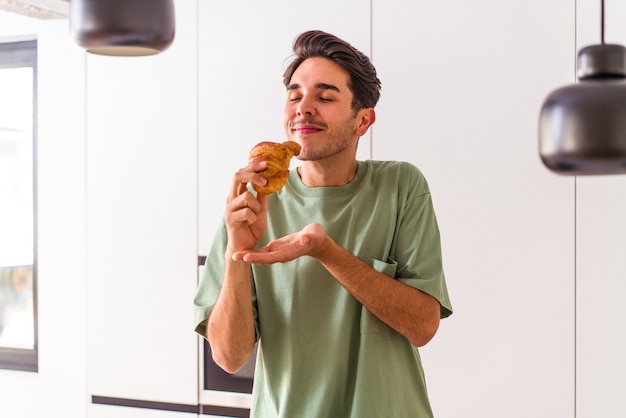 Un joven de raza mixta comiendo croissants en una cocina por la mañana