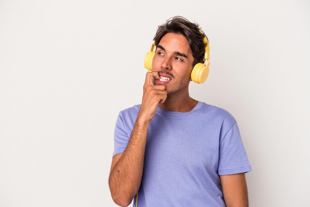 Un joven de raza mixta escuchando música aislado de fondo azul se relajó pensando en algo mirando un espacio de copia.